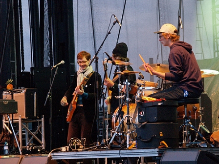 The Whitest Boy Alive, im linken Bildrand am Verstärker eine Ananas, in der Bildmitte der Sänger, der Bassist. Rechts davon der SChlagzeuger. 